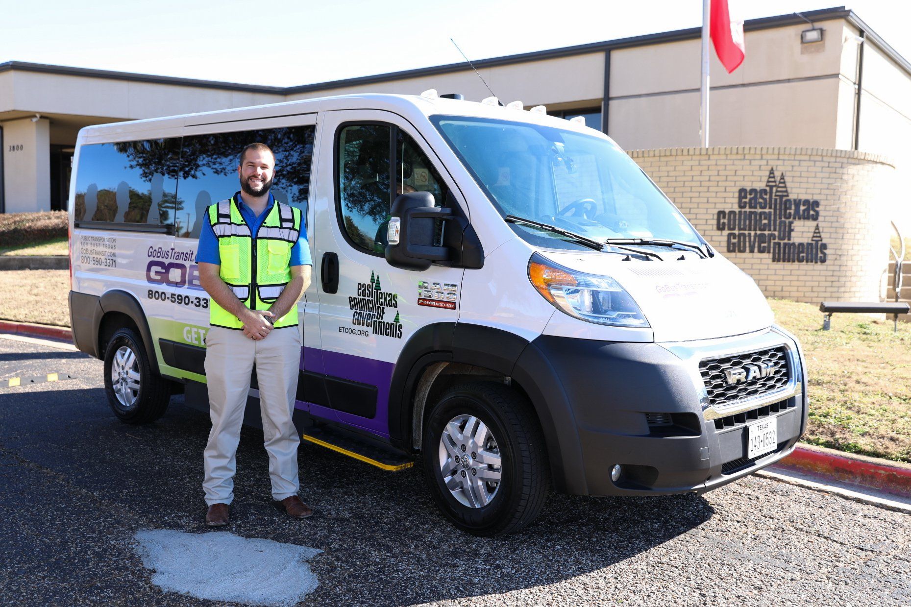 A man in a yellow vest is standing in front of a van.