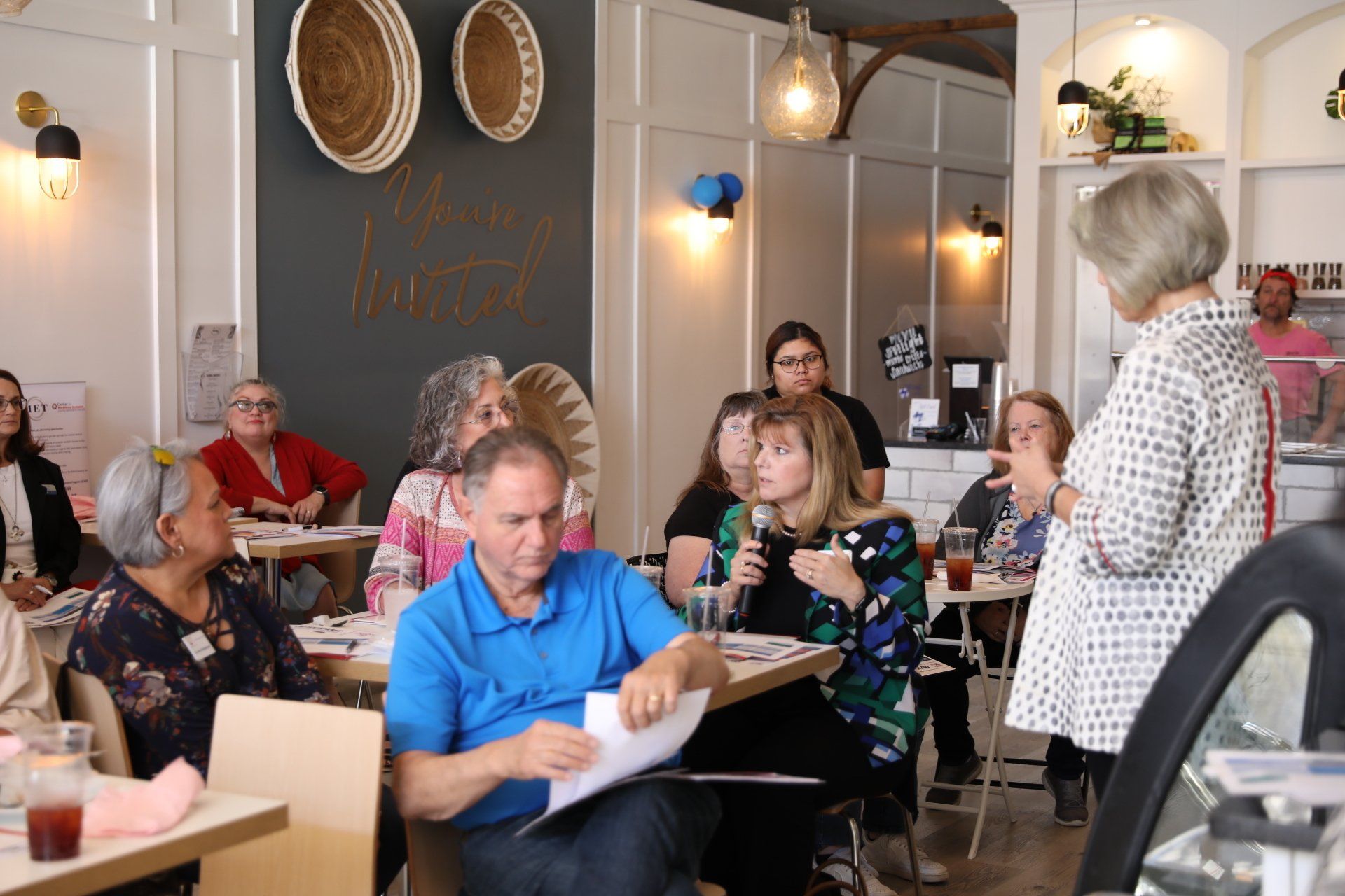 A woman is giving a presentation to a group of people sitting at tables in a restaurant.