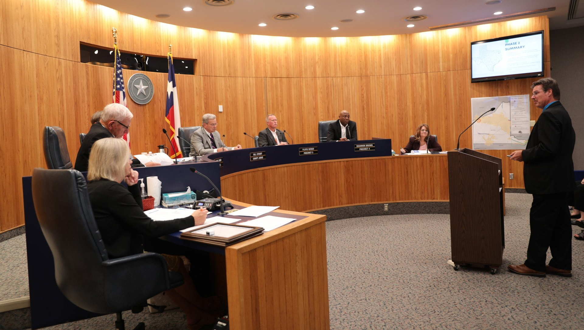 A man is giving a speech in front of a group of people in a board room.