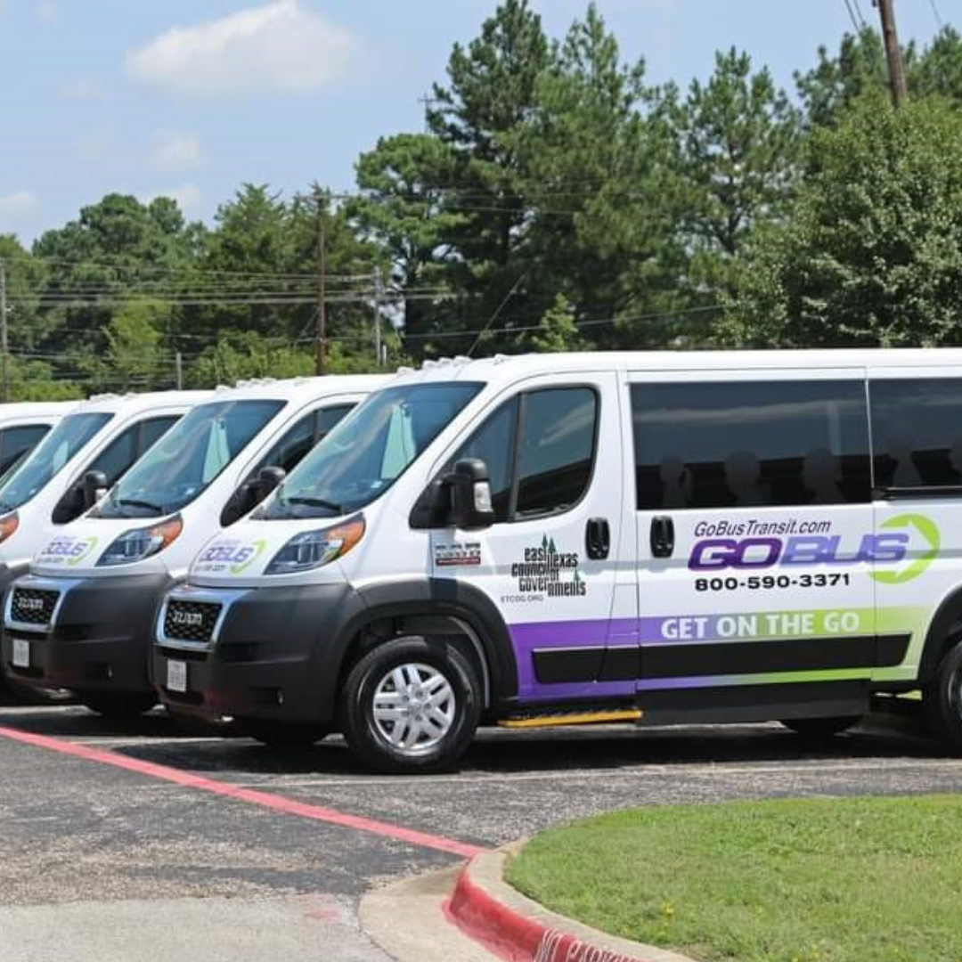 Three white C2G shuttle vans parked in a row on a curbside lot