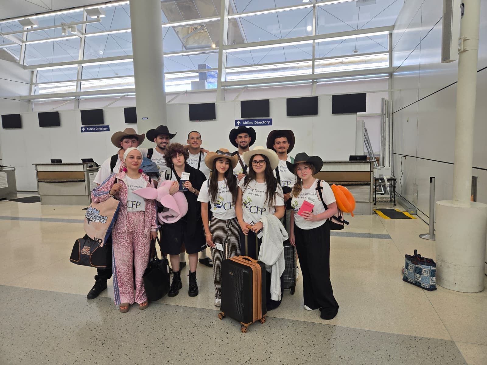 Group of people in cowboy outfits posing with suitcases in a bright airport terminal