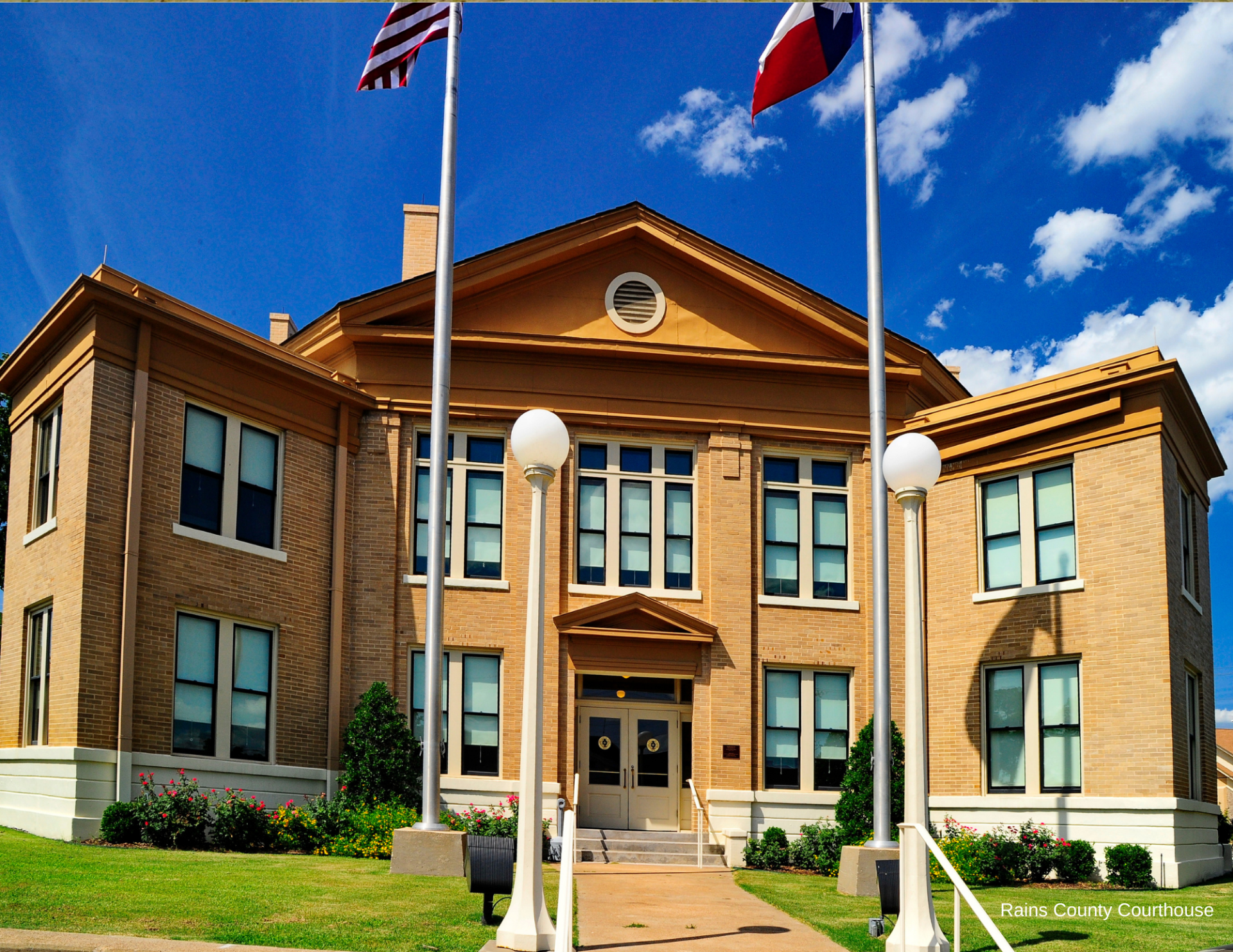 Historic brick civic building with columns, flags, and a central entrance under a blue sky.