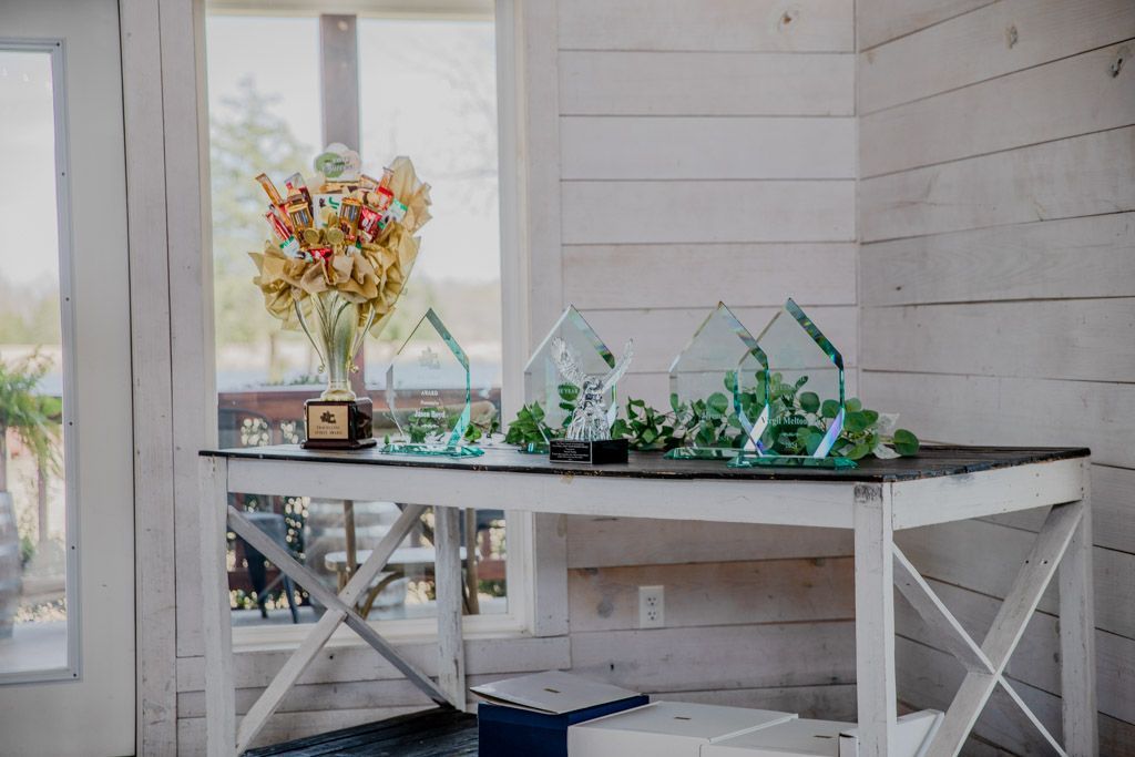 White table with awards, floral arrangement, and greenery against a white wooden wall.