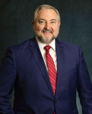Smiling man in a navy suit with a red striped tie against a dark studio background