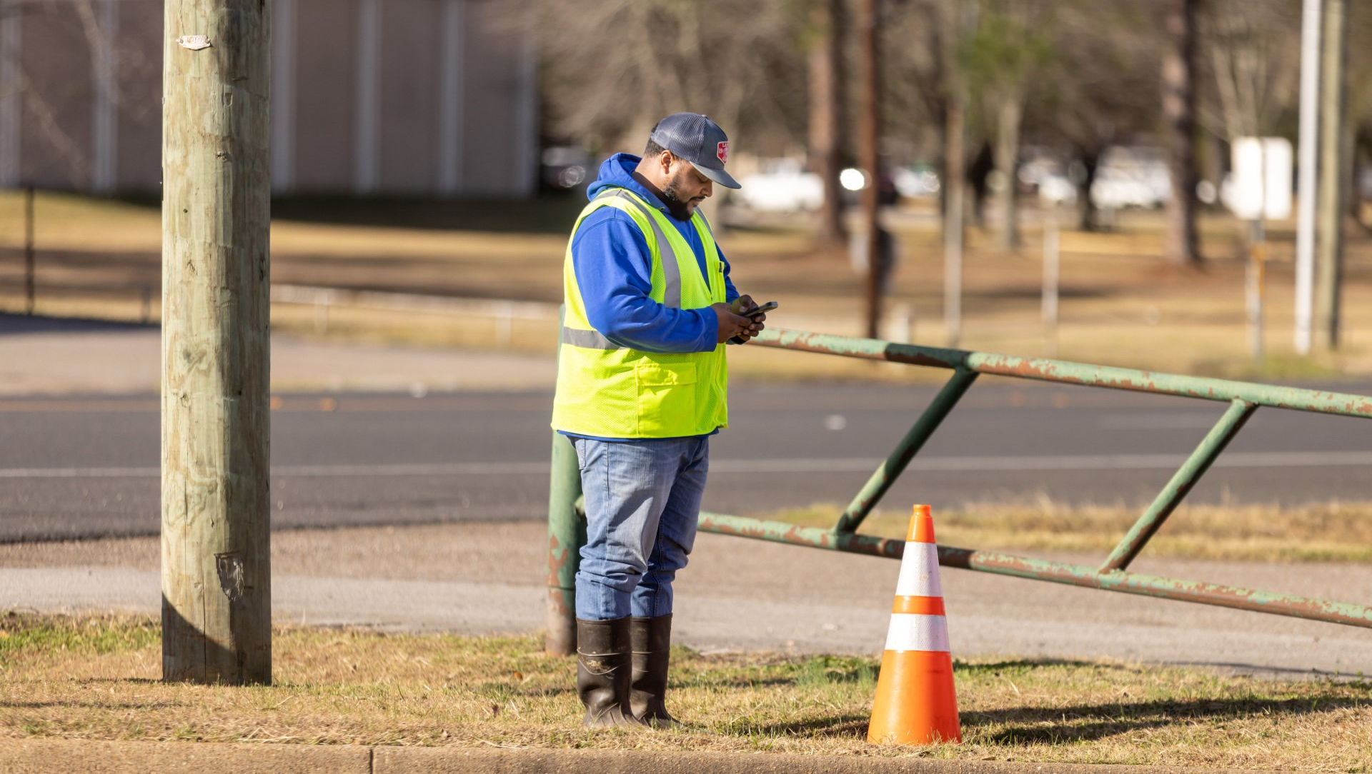 A man in a yellow vest is standing next to a traffic cone on the side of the road.