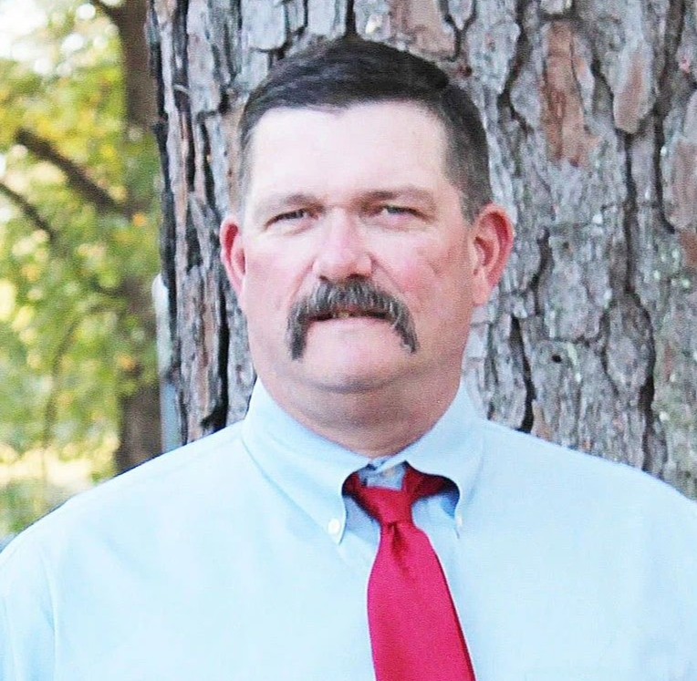 Portrait of a man in a light blue shirt and red tie standing by a tree