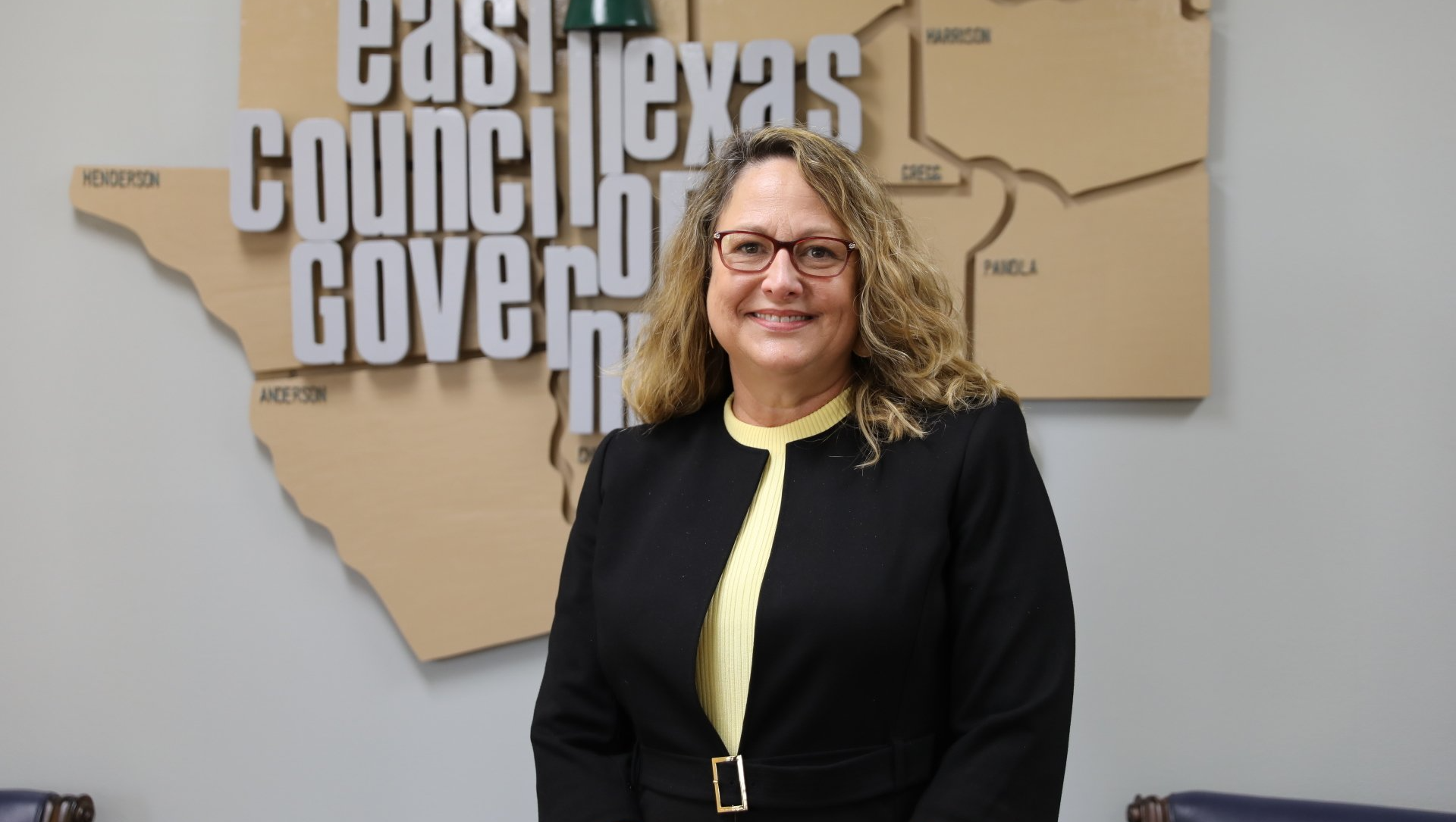 A woman in a black jacket is standing in front of a map of texas.