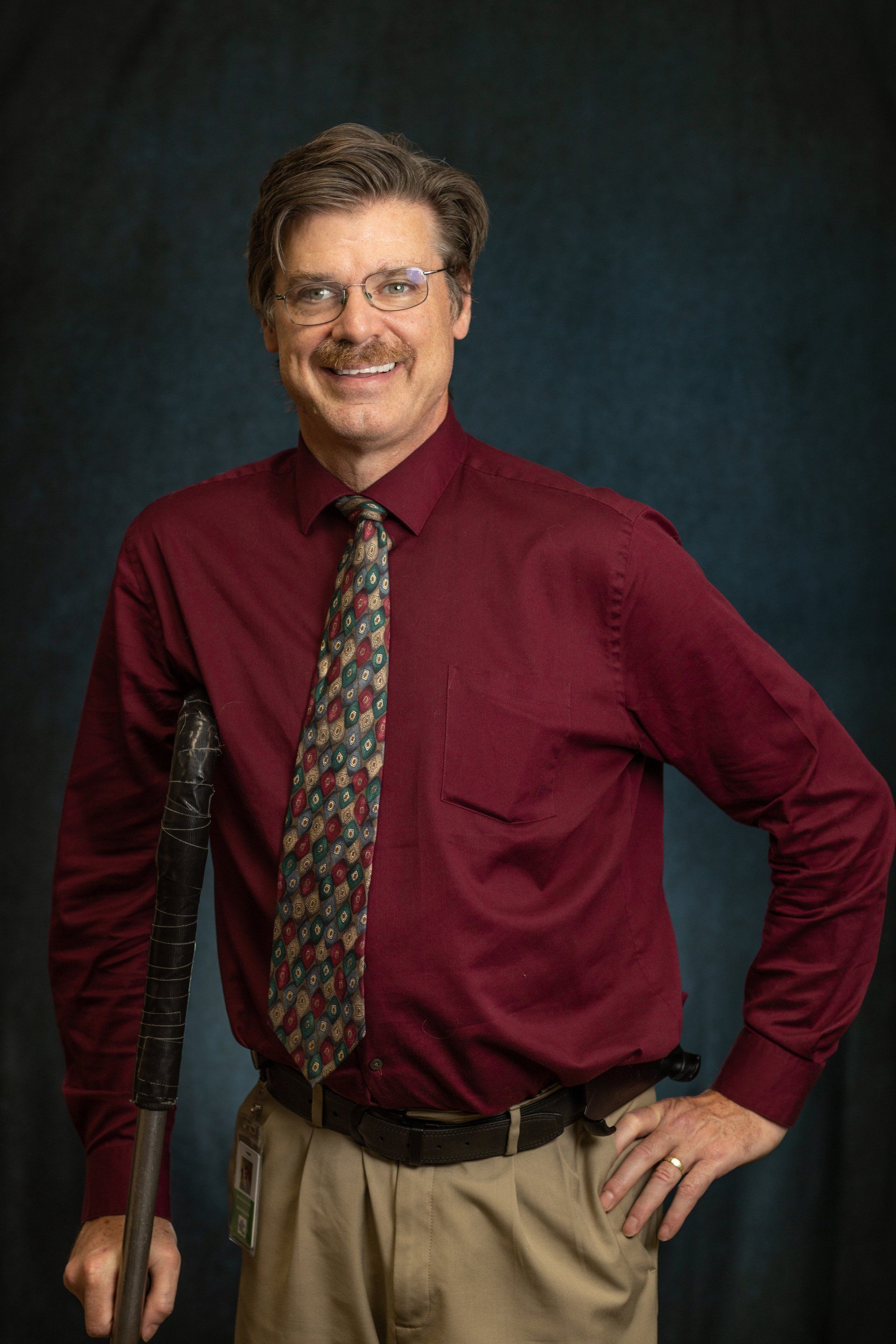 A man in a red shirt and tie is holding a cane.
