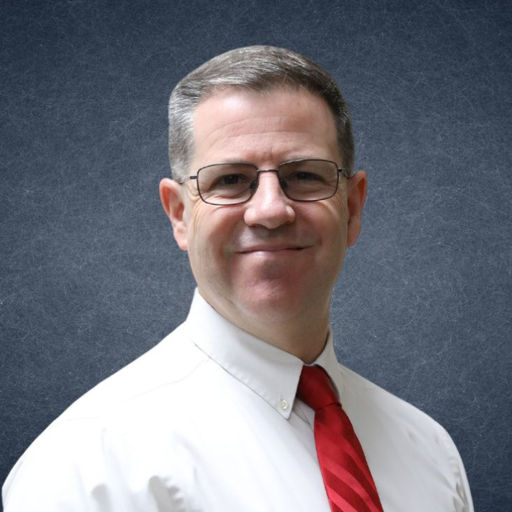 Portrait of a smiling man in glasses, white shirt, and red tie against a gray backdrop