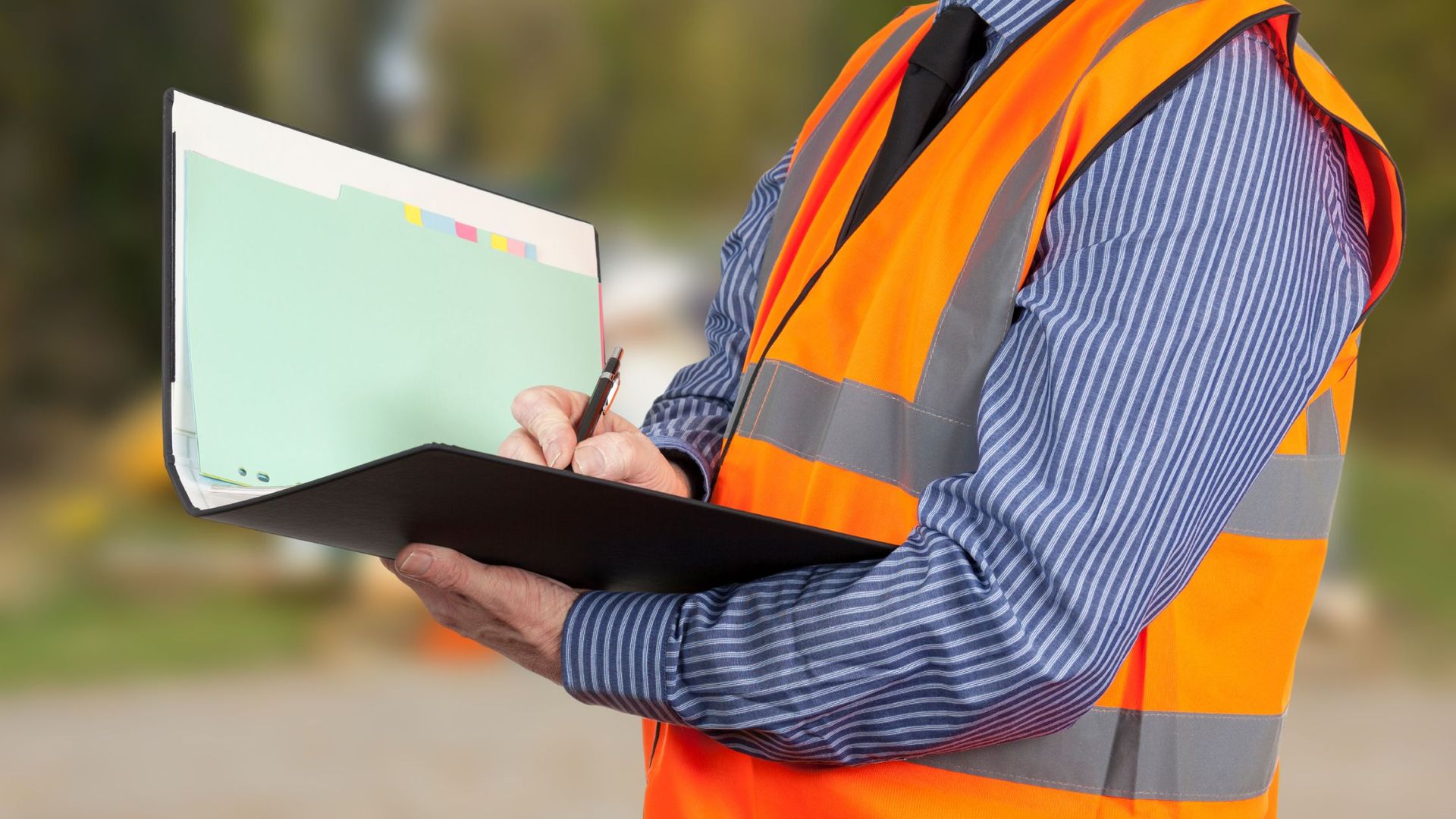 A man in a safety vest is writing on a clipboard.