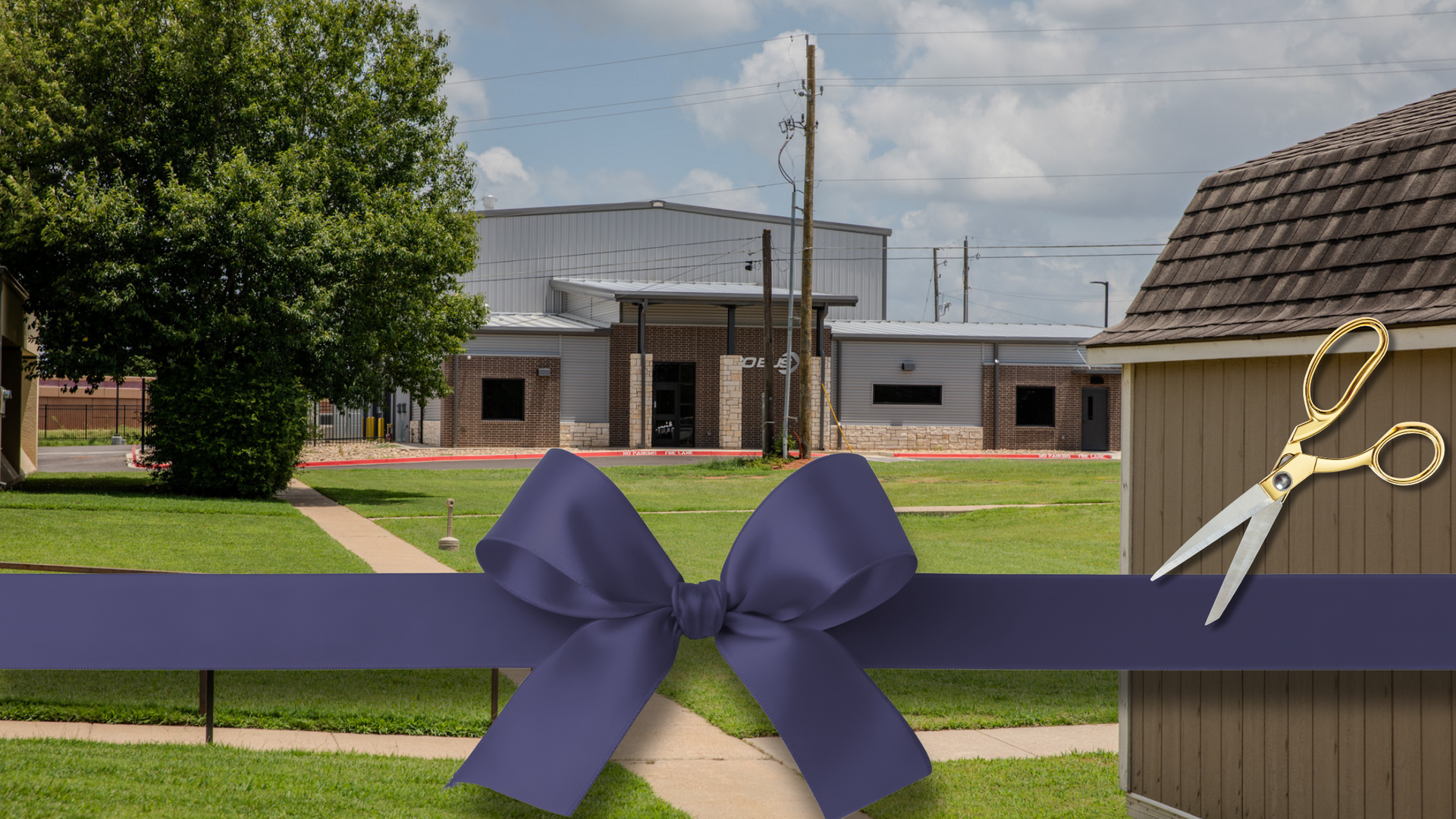 Ribbon-cutting ceremony with purple bow and gold scissors in front of a light-colored building and green lawn.
