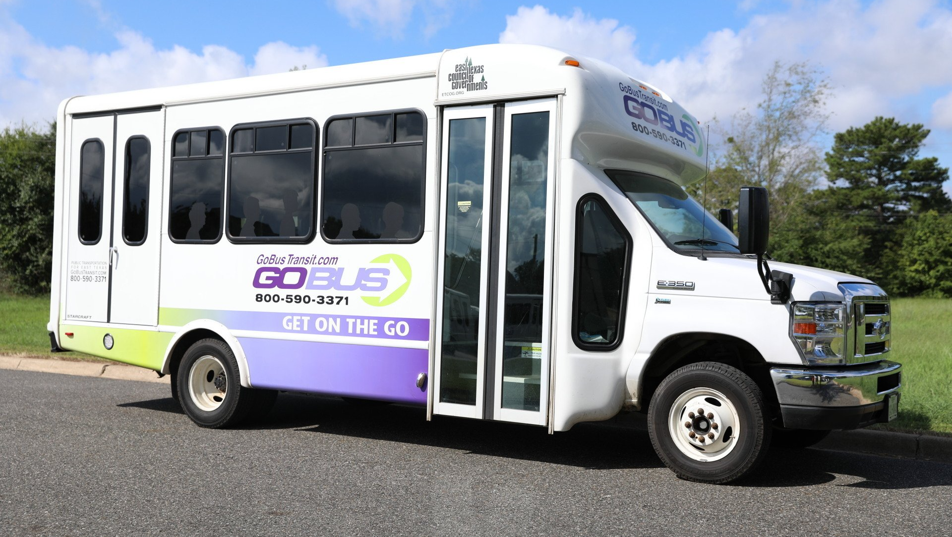 A white and purple bus is parked on the side of the road.