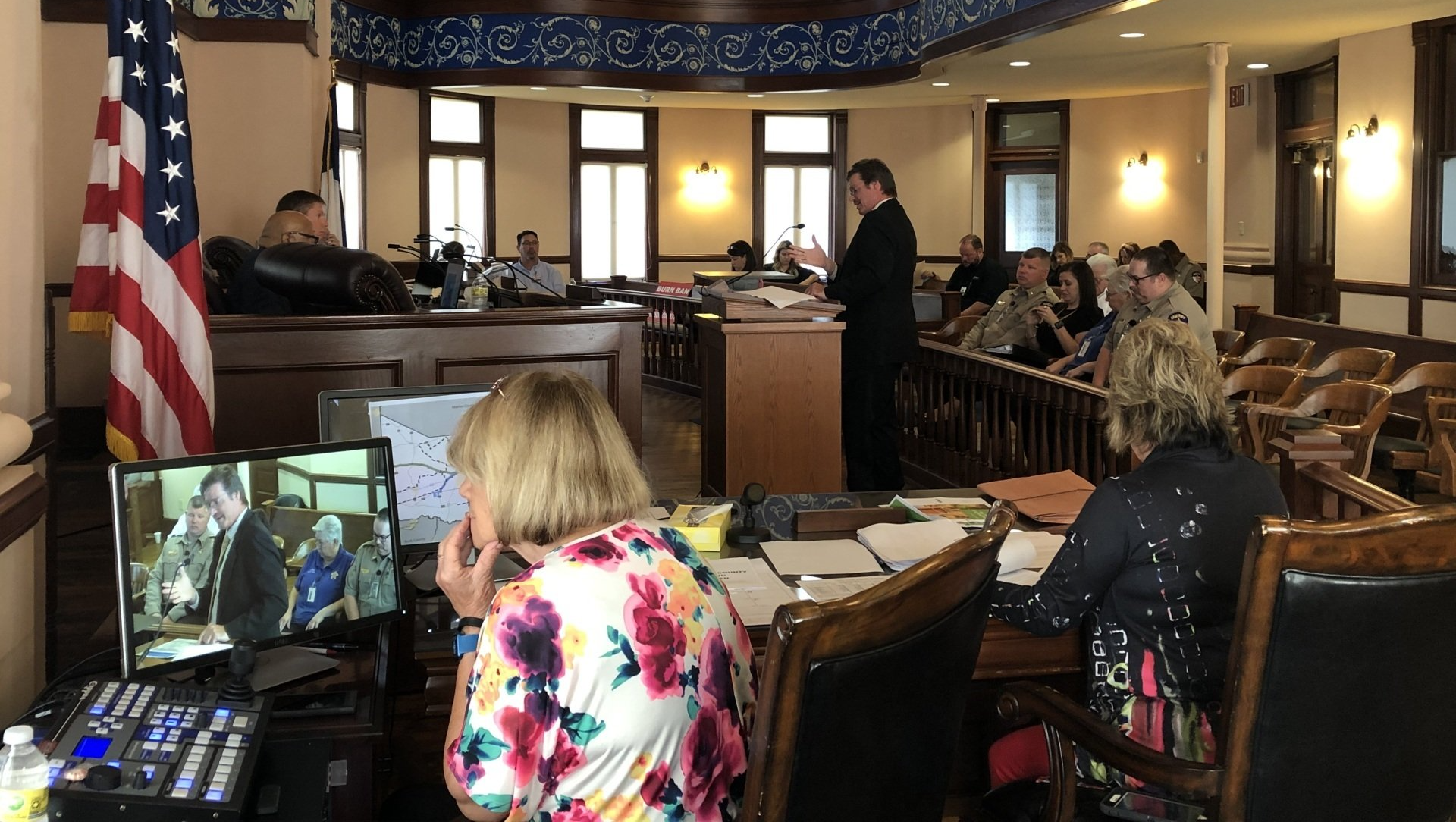 A woman is sitting at a desk in a courtroom talking on a cell phone.