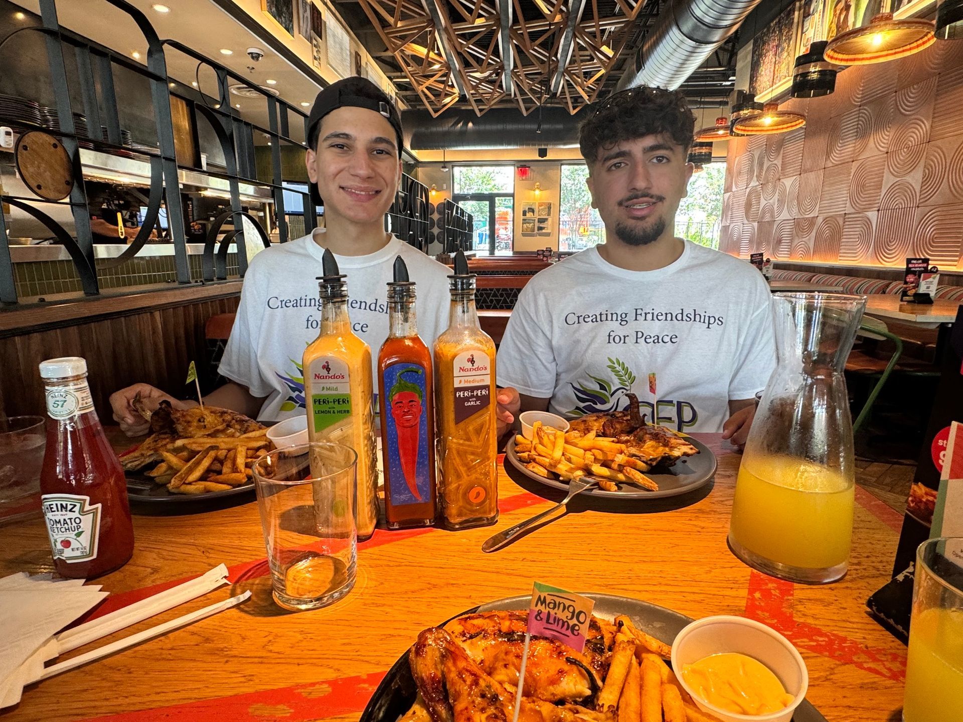 Two friends at a restaurant table with burgers, fries, drinks, and sauces in a warm, rustic interior.