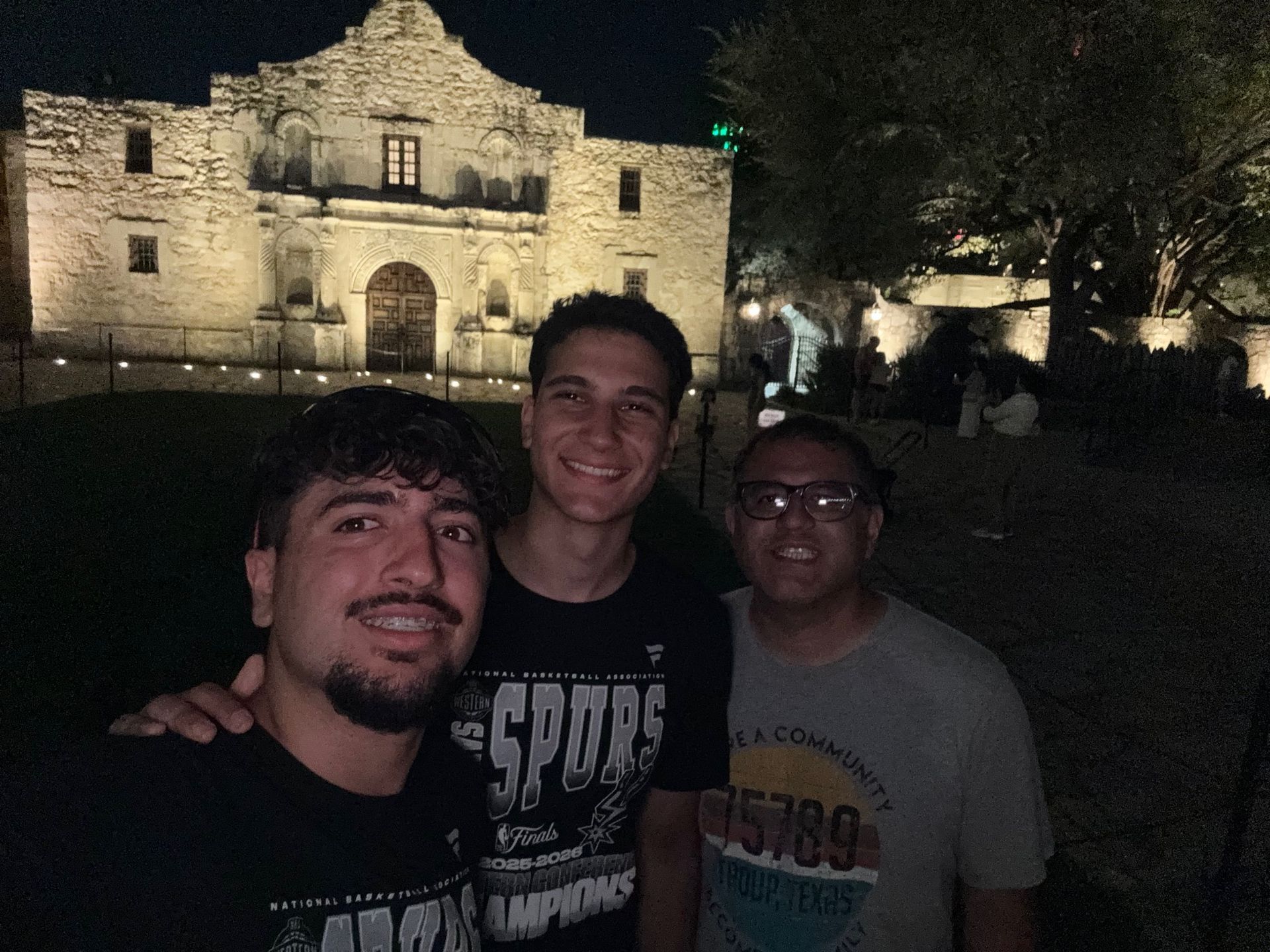 Three people smiling in front of a lit stone building at night