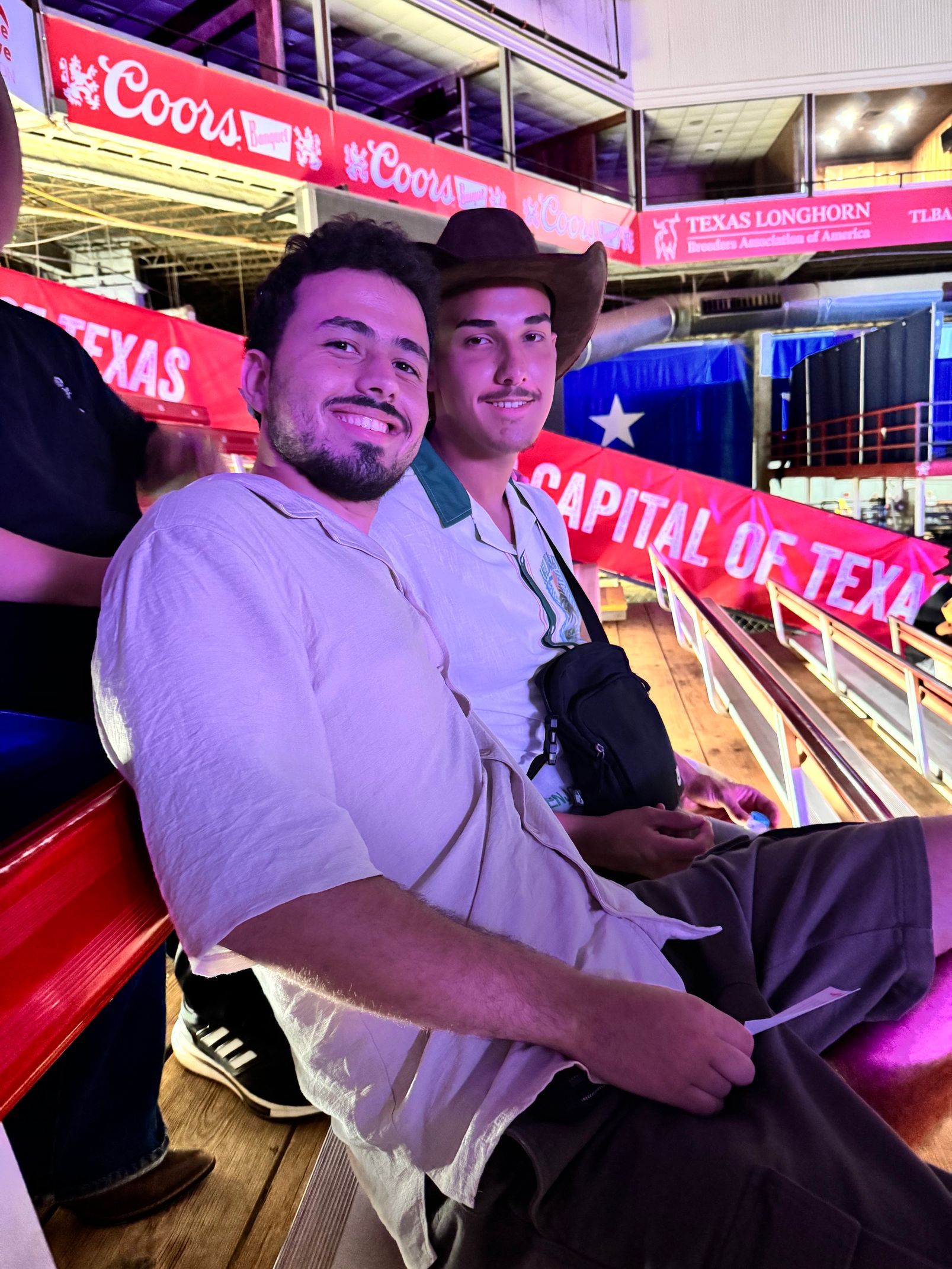 Two men sitting on a red-lit ride with “Capital of Texas” signs in the background