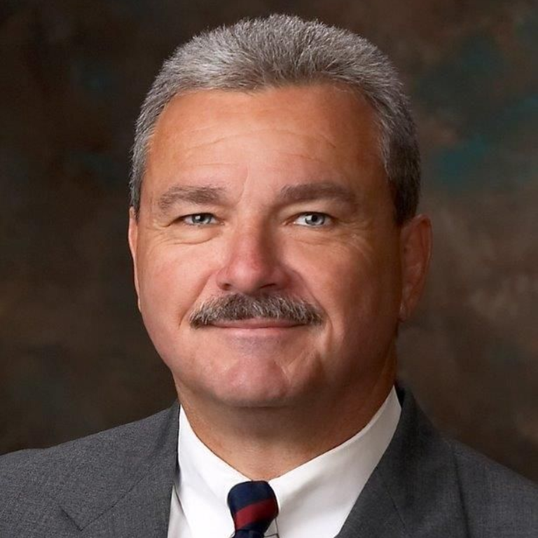 Smiling man in glasses wearing a blue suit and red tie outdoors