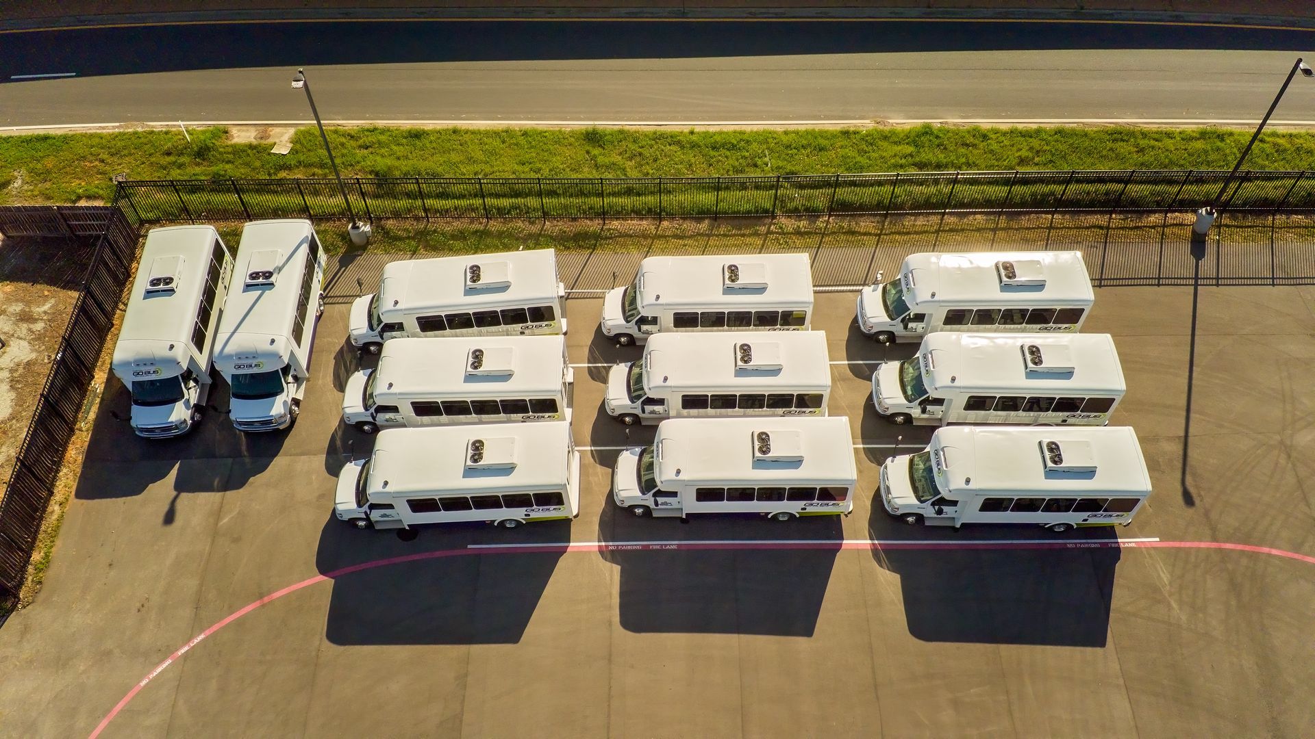 Aerial view of several white RVs parked in neat rows beside a road and sidewalk.