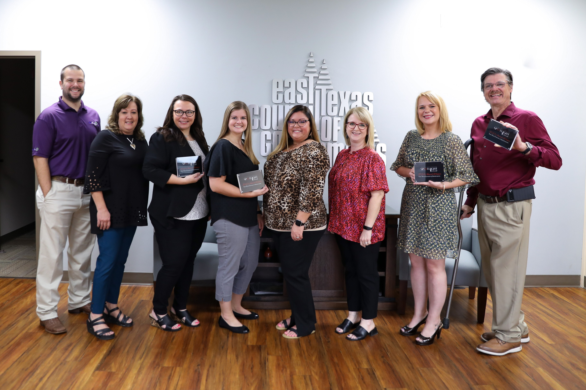 A group of people standing next to each other in a room holding awards.