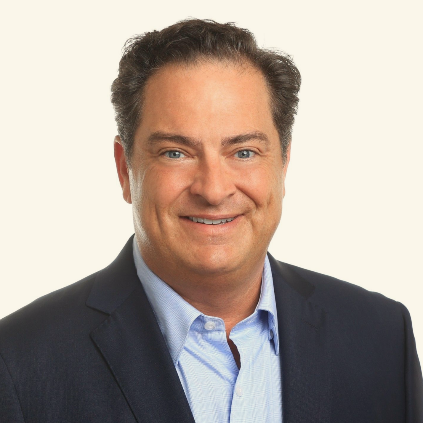 Portrait of a smiling man in a dark blazer and light blue shirt on a neutral background
