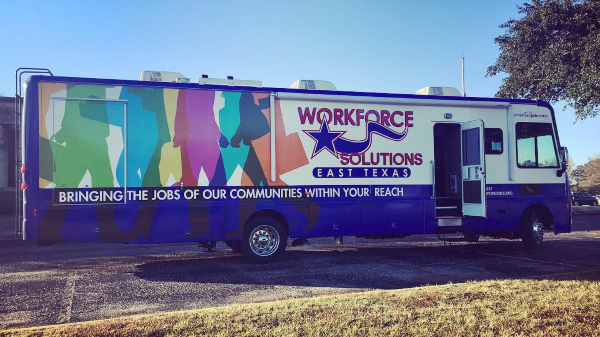 A blue workforce solutions bus is parked in a grassy area