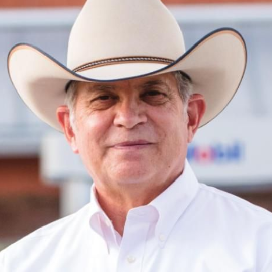 Portrait of a smiling person in a white cowboy hat and white shirt outdoors