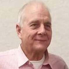 Smiling man in a pink checkered shirt against a plain wall
