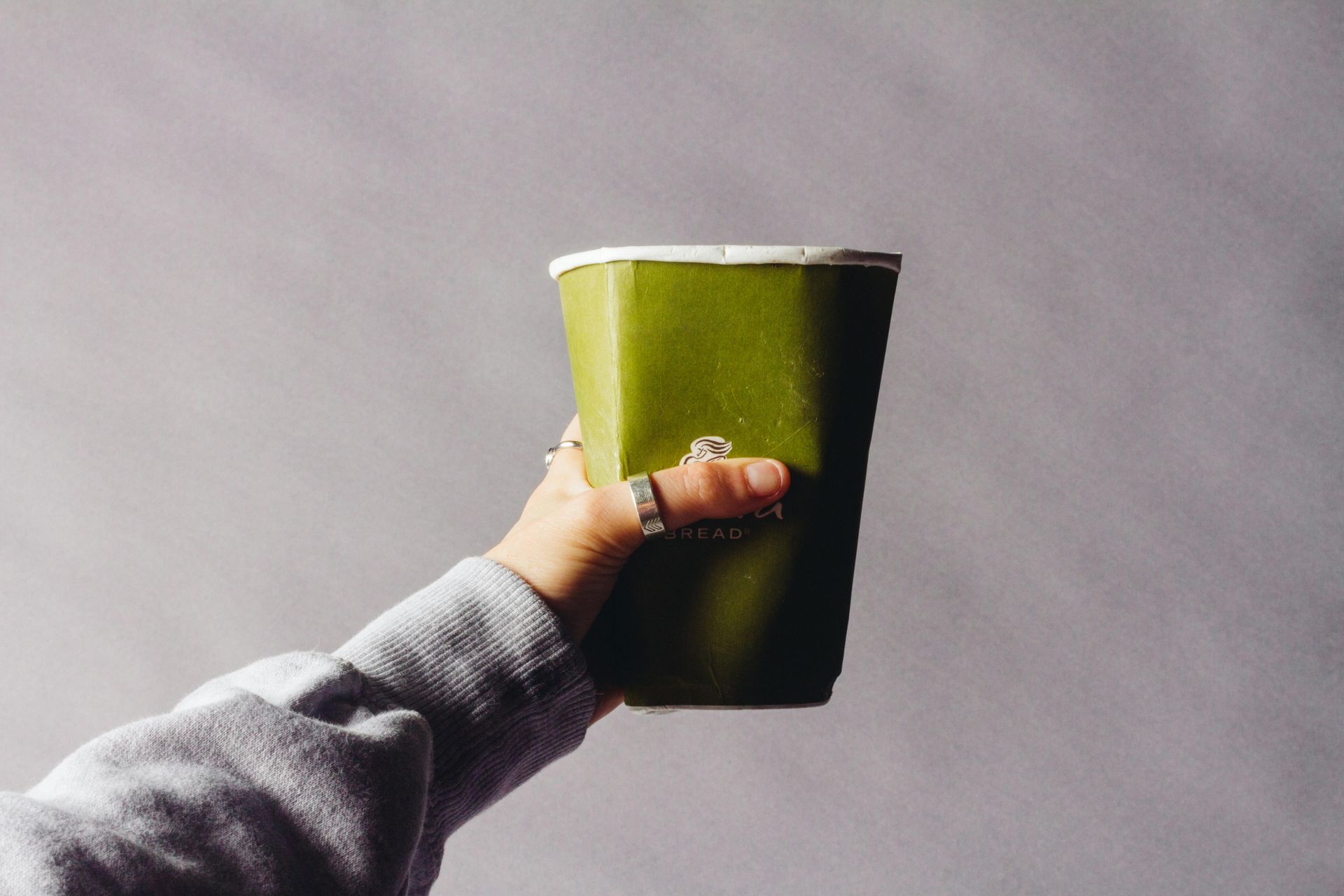Person's hand holding a green cup, angled up; against a gray background.