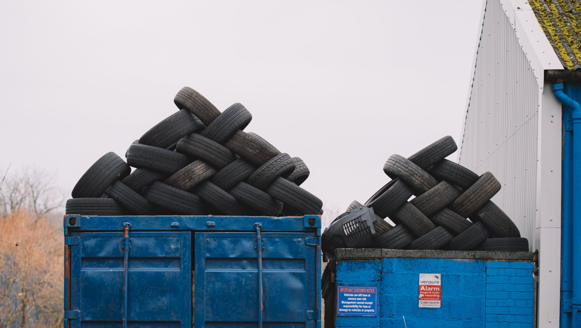 A pile of tires is sitting on top of a blue dumpster.