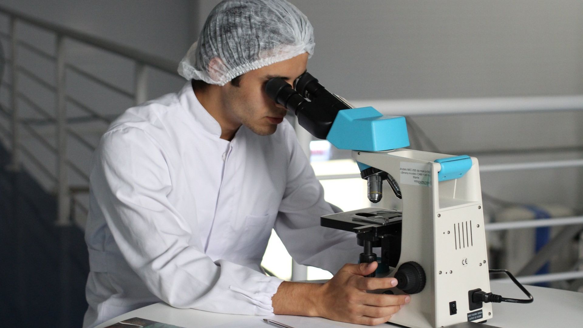 A man in a lab coat is looking through a microscope.