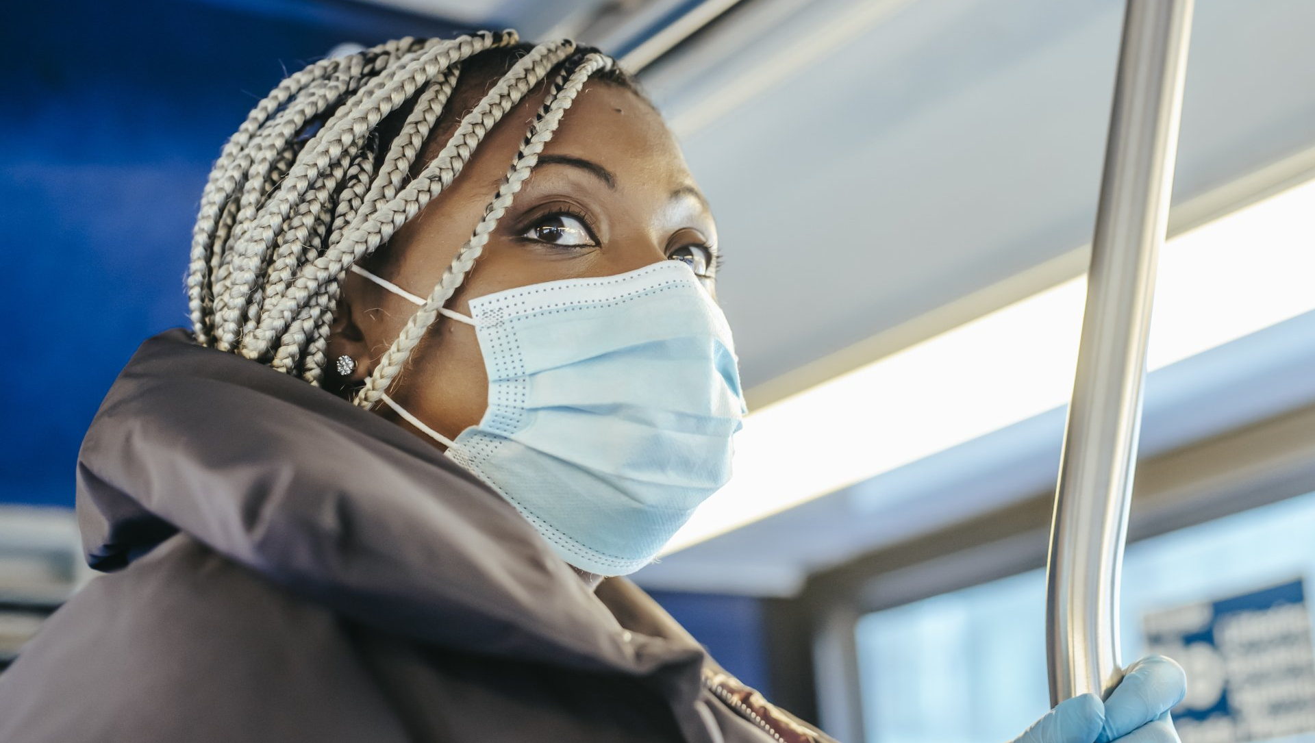 A woman wearing a face mask is riding a bus.