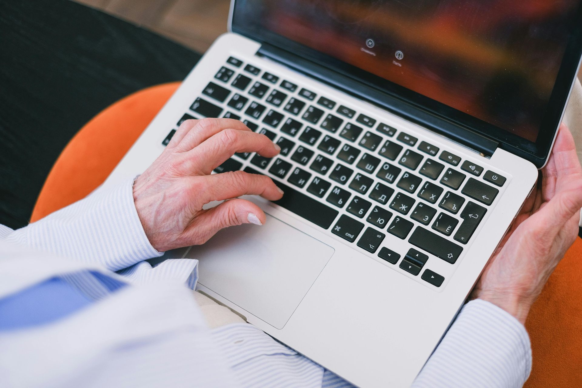 Hands typing on a laptop keyboard while resting on an orange surface.
