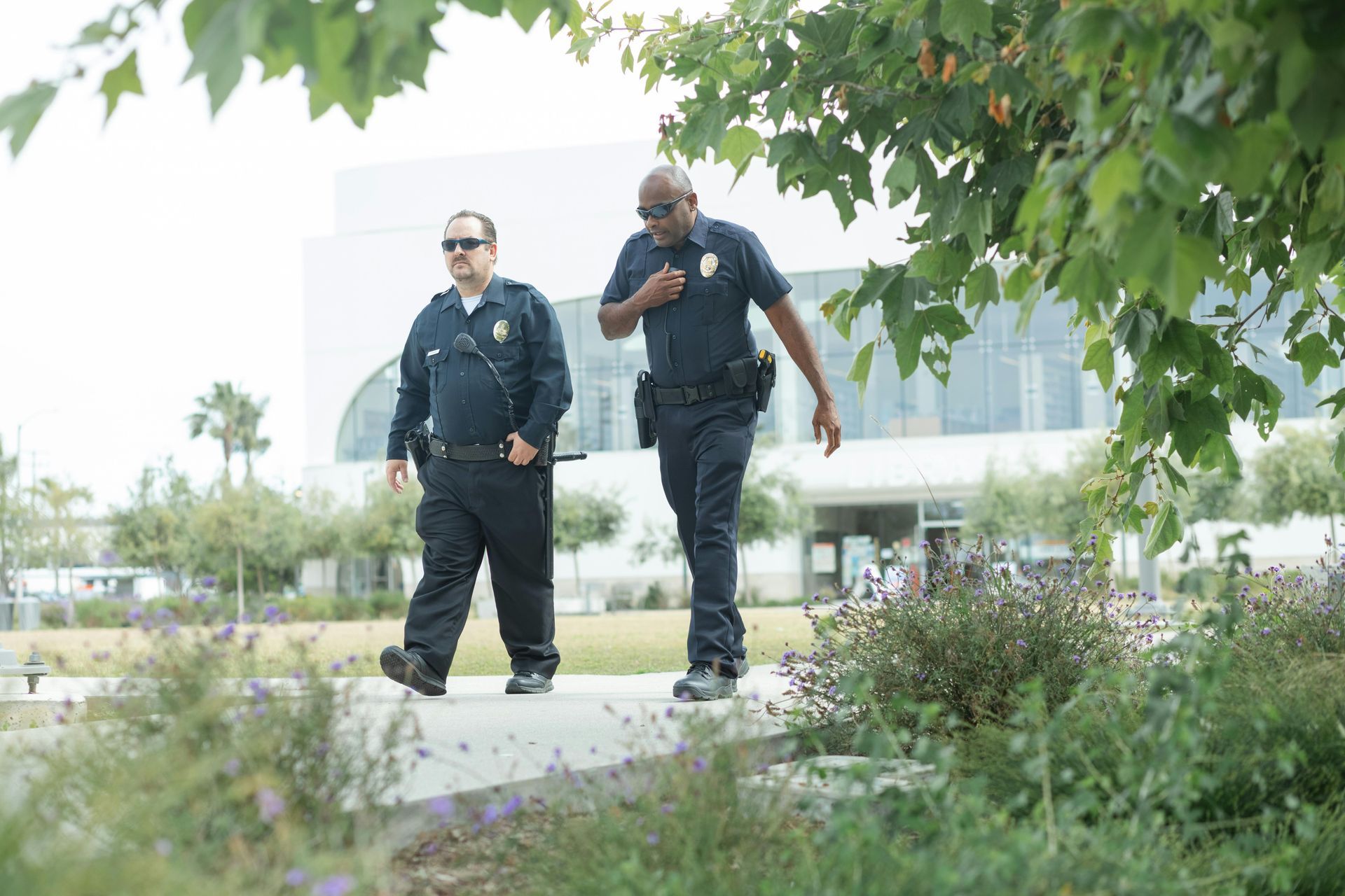 Two uniformed police officers walking outdoors near a modern building.