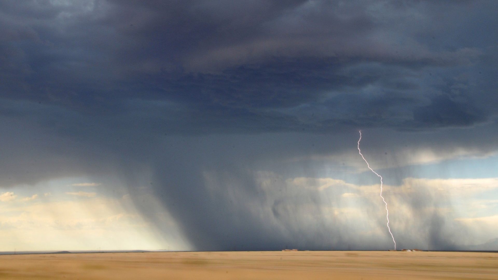 Dark storm cloud over a flat plain with a visible tornado and lightning strike on the right