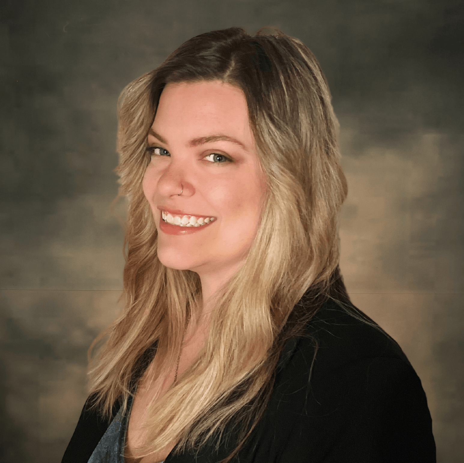 Smiling woman with long blonde hair in a black top against a soft studio backdrop