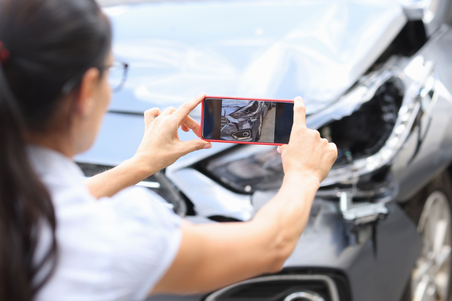 A person taking a photo of a damaged vehicle with a smartphone, documenting evidence after a car accident.