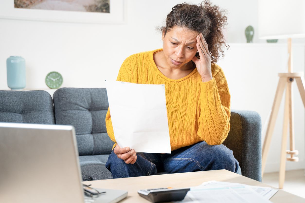 A grieving woman sitting on the couch reviews a life insurance denial letter.