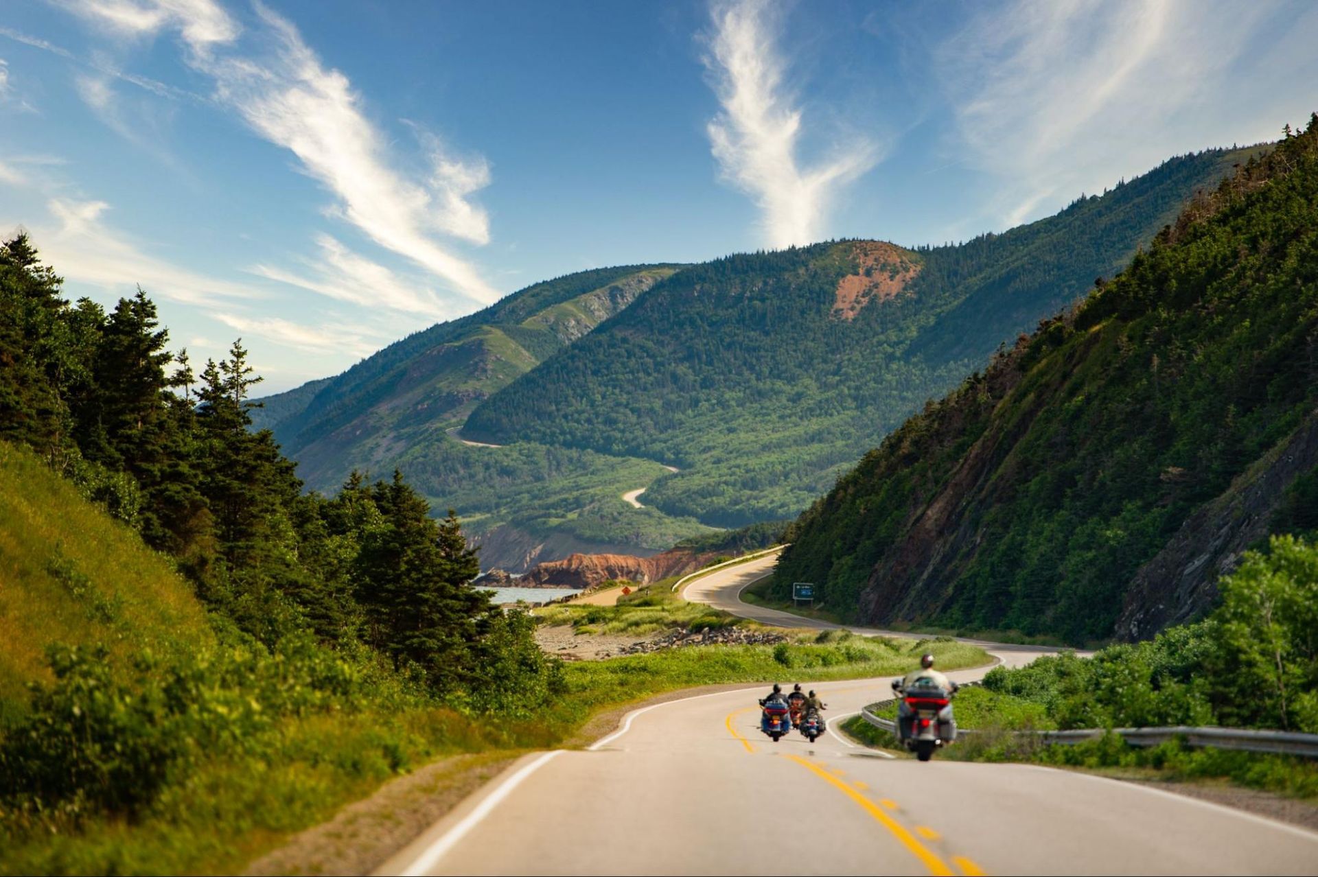 Three motorcycles and their riders on a road in the summer.