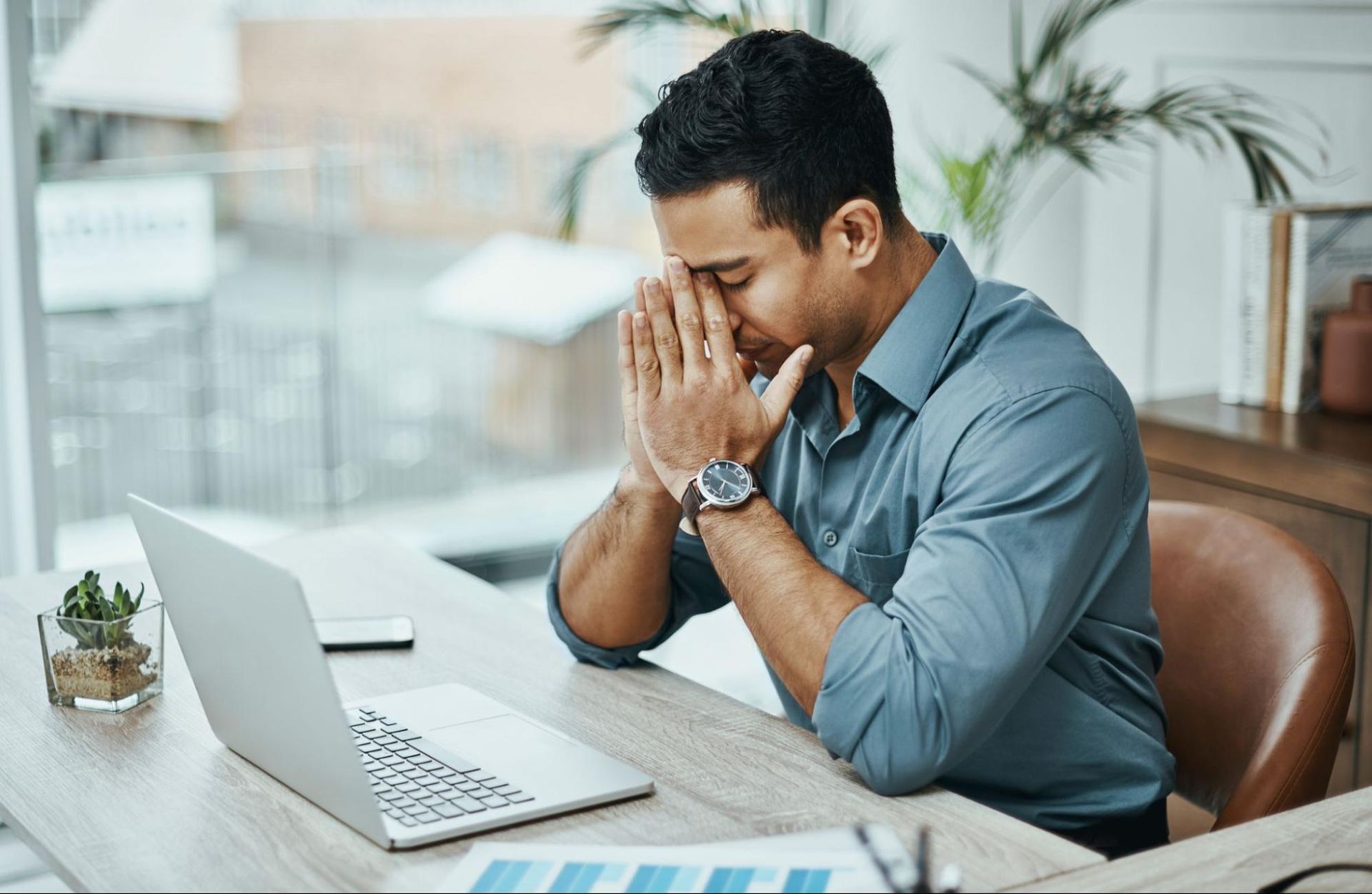 Man sitting at a desk with head in hands, looking upset.