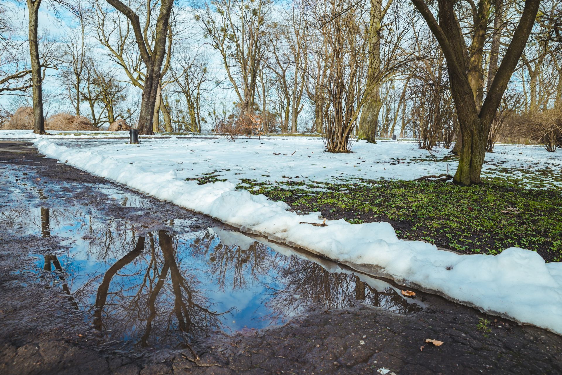 A thawing park pathway with melting snow and puddles, illustrating springtime slip-and-fall hazards.