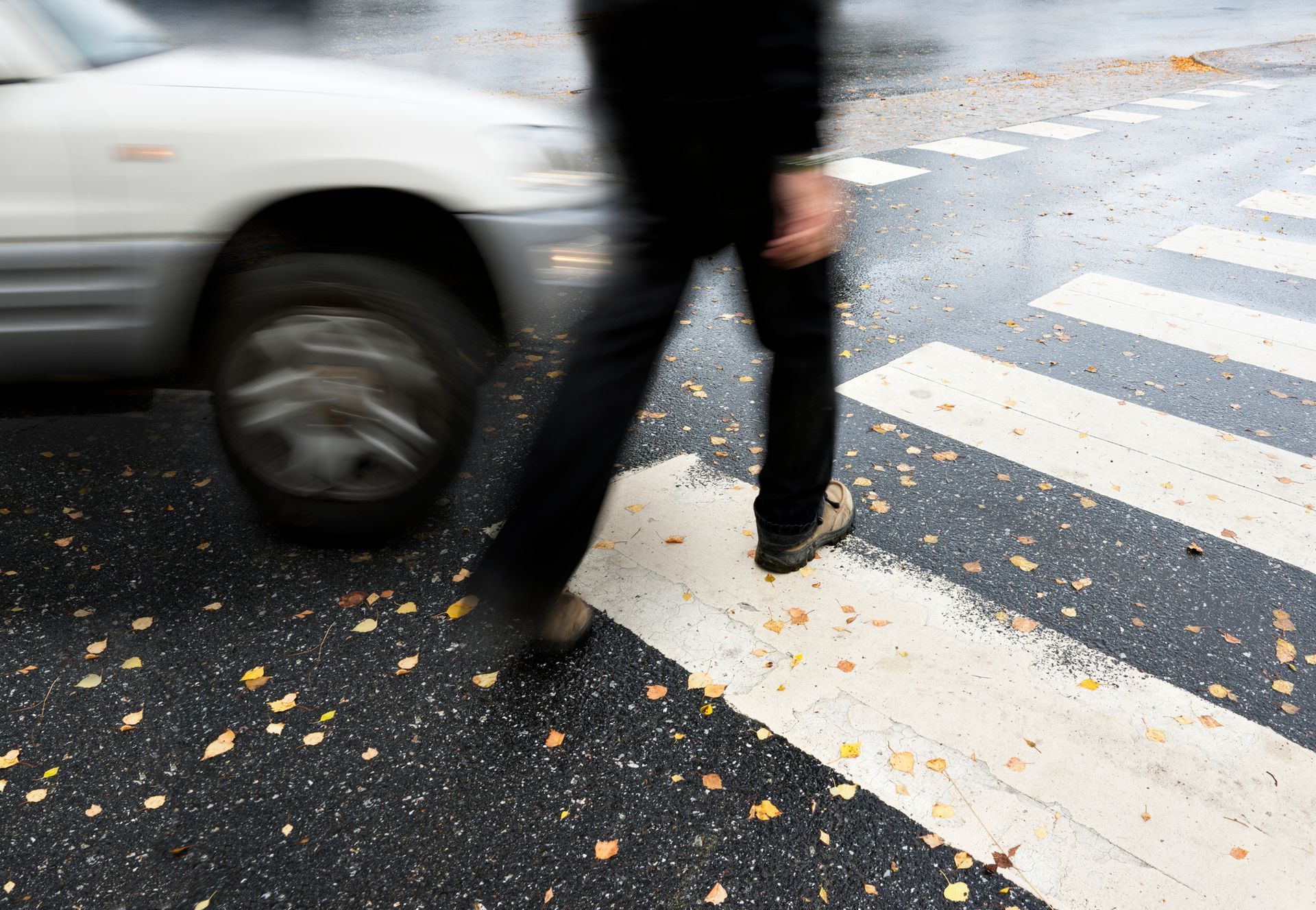 A pedestrian crossing the street as a car approaches, capturing a potential accident scene in motion