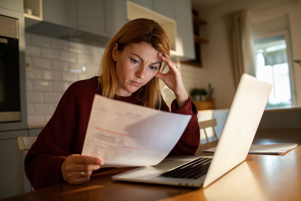 A concerned woman reviewing a denied life insurance claim letter while sitting at her kitchen table with a laptop.