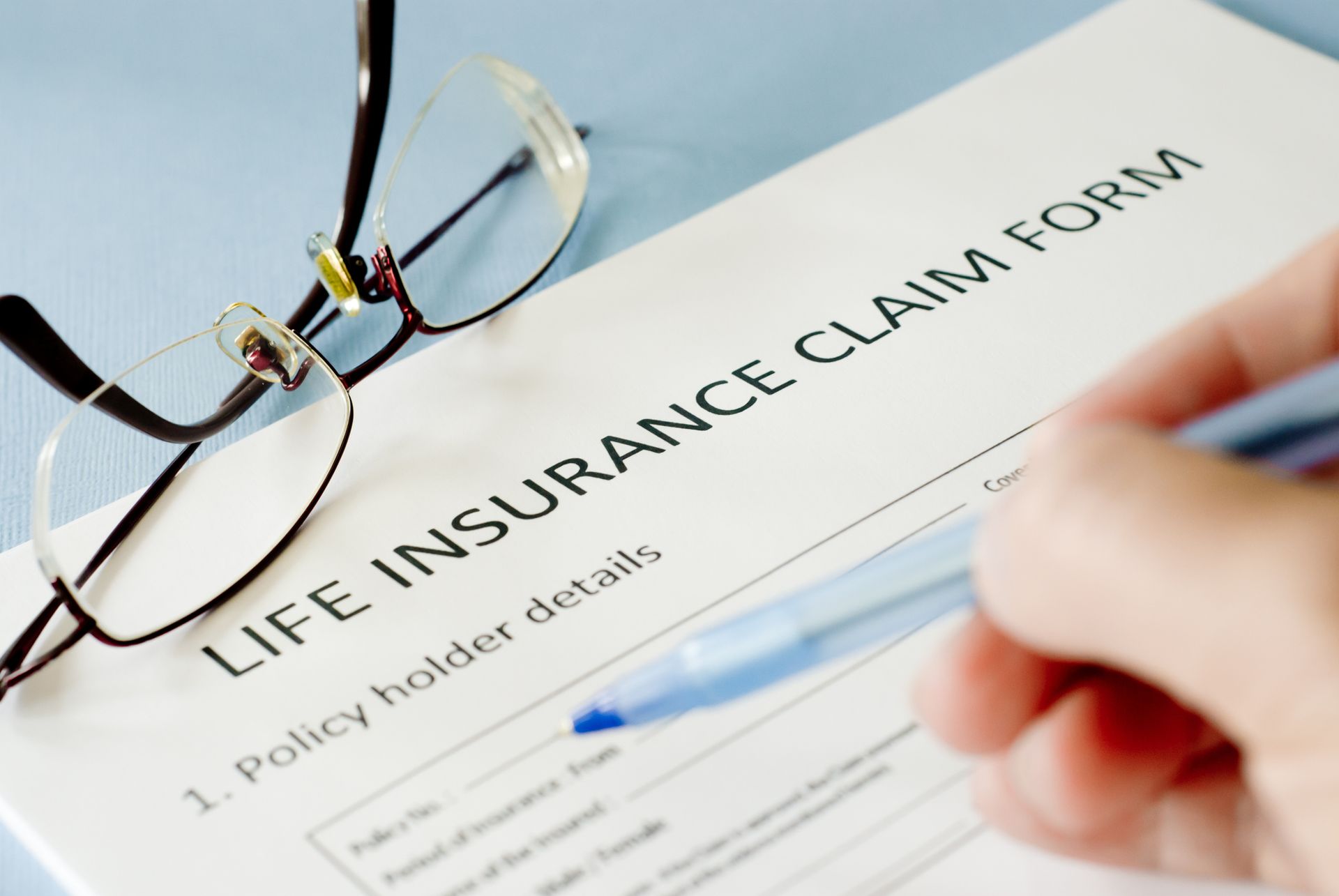 A life insurance claim form with a pen and eyeglasses placed on it, representing the process of filing a life insurance claim.