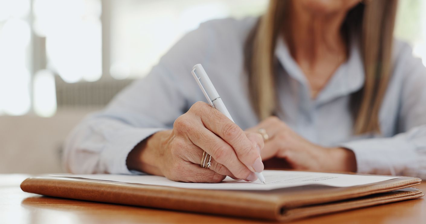 A woman sitting at a table fills out a life insurance application form, an instance where obtaining the support of a life insurance claim lawyer may be beneficial.