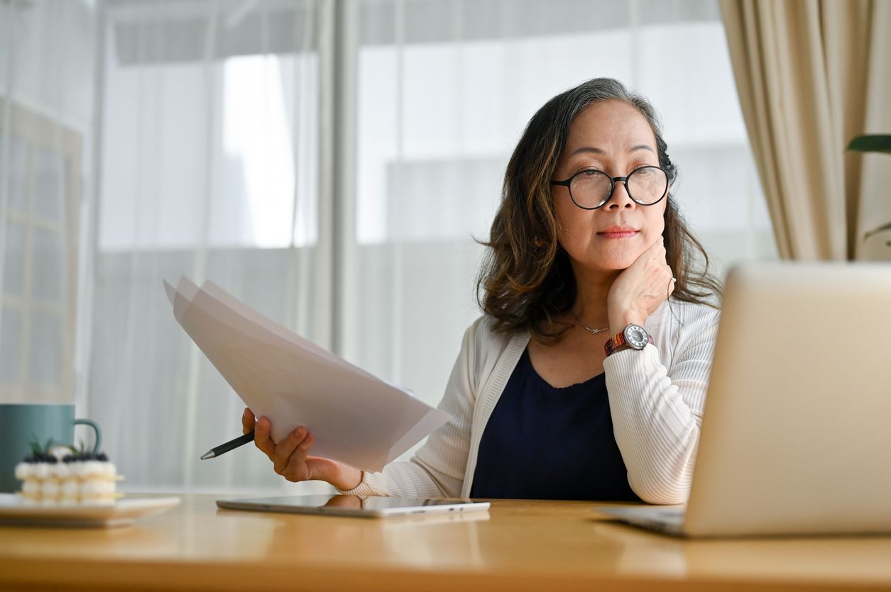 A woman sits at a desk at home, looking at her laptop