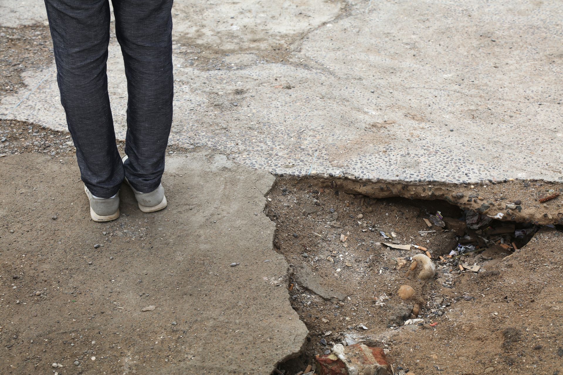 Close-up of a damaged and uneven sidewalk with a person standing near the edge, illustrating a potential slip and fall hazard.