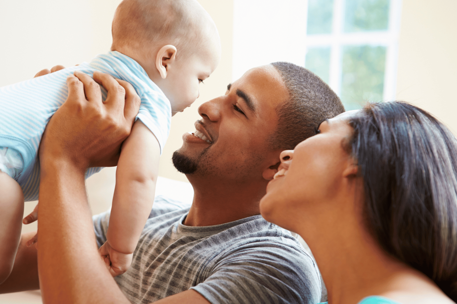 Family sharing a warm embrace on a couch, with a baby reaching toward a smiling man and woman.