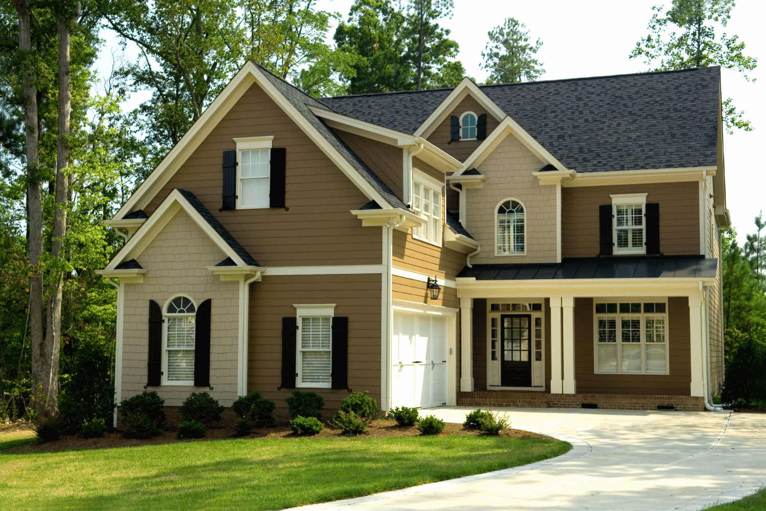 Suburban two-story beige house with brown shutters, front porch, and a curved driveway