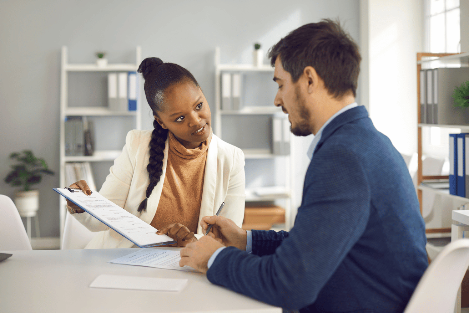 Two coworkers discussing documents at a desk in a bright office