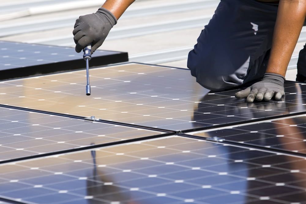 A Man Is Installing Solar Panels on A Roof with A Screwdriver — Eco Sparks Solar & Electrical Contractors in Berrimah, NT